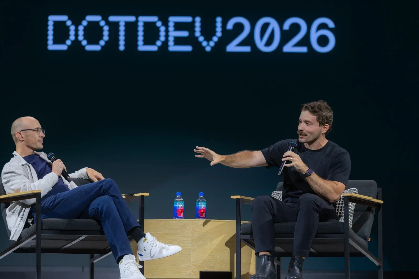 Fireside chat, ο ένας καθισμένος άνδρας χειρονομεί προς τον άλλον καθώς κρατούν μικρόφωνα